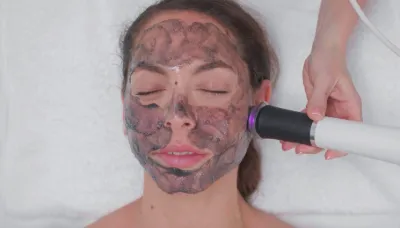 A client during a facial with a dark treatment mask and a handheld device